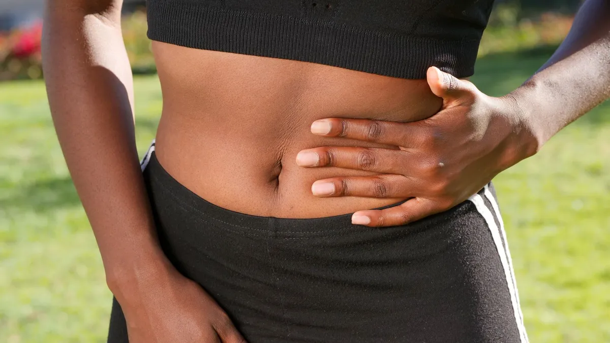 Close-up of a person holding their abdomen, showing abdominal area.