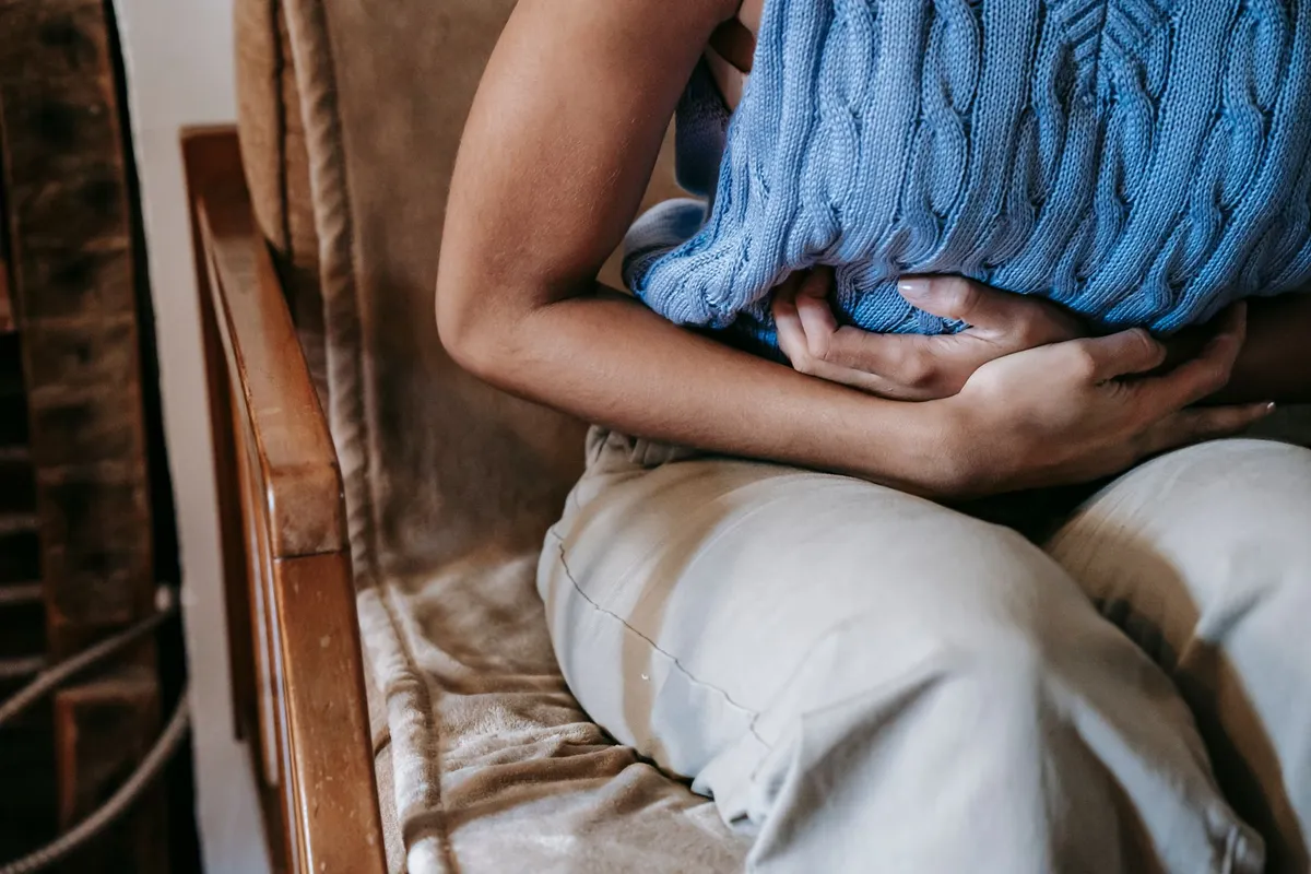 Child holding stomach while sitting on a couch, indicating abdominal pain.