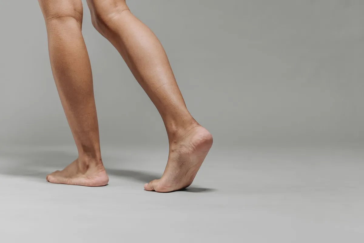 Bare feet showing the Achilles tendon area while walking on a gray surface.
