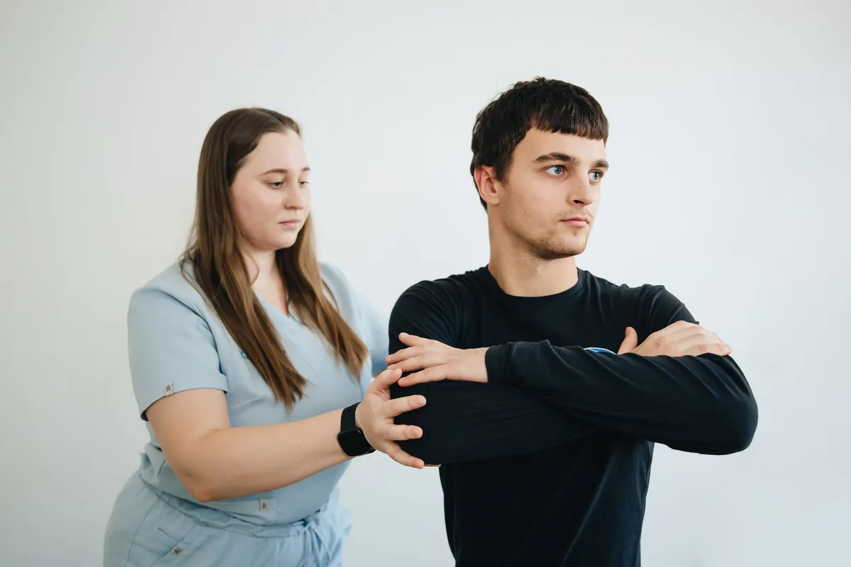 Physical therapist assisting a man with arm stretching exercises in a clinical setting.