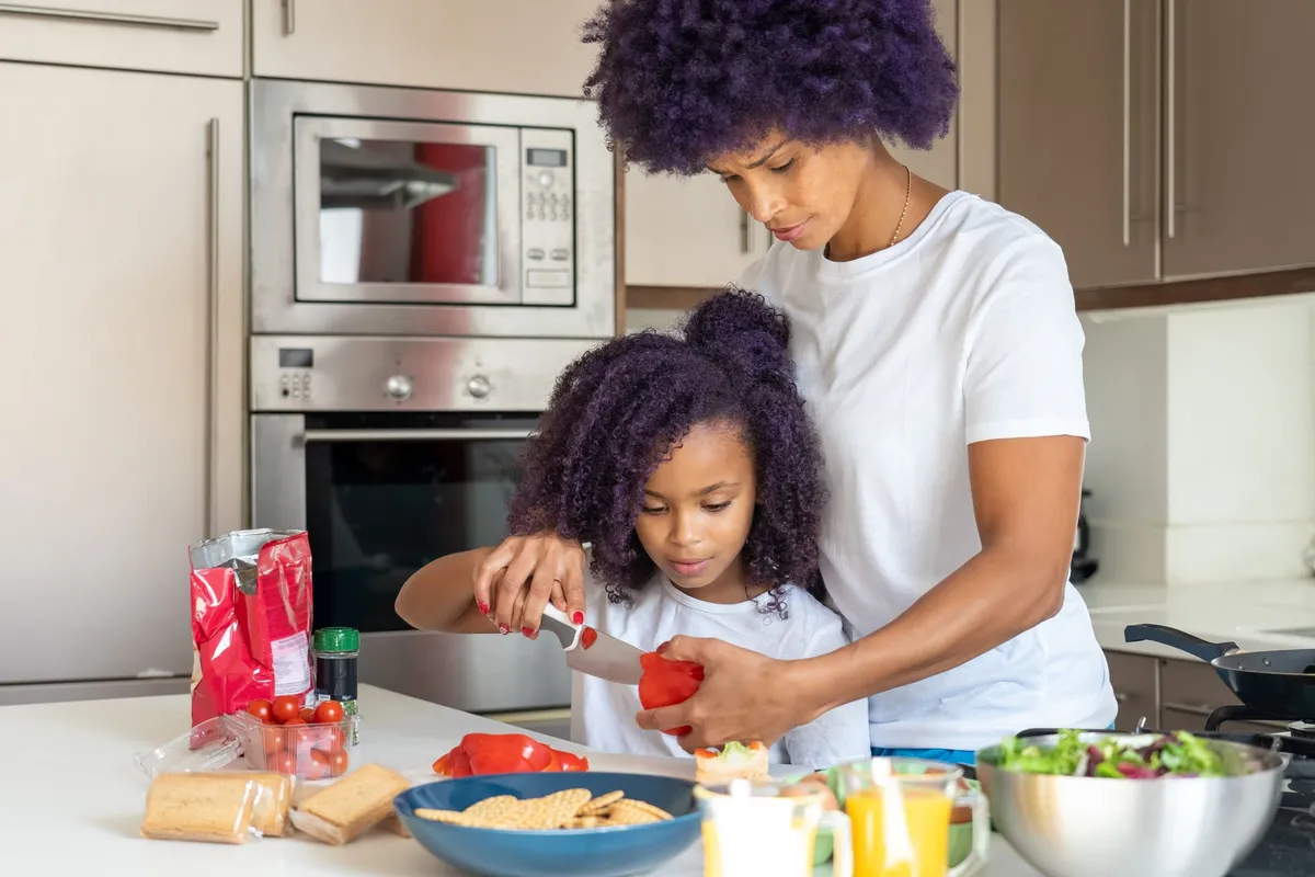 A mother and daughter preparing healthy snacks with vegetables in a kitchen.