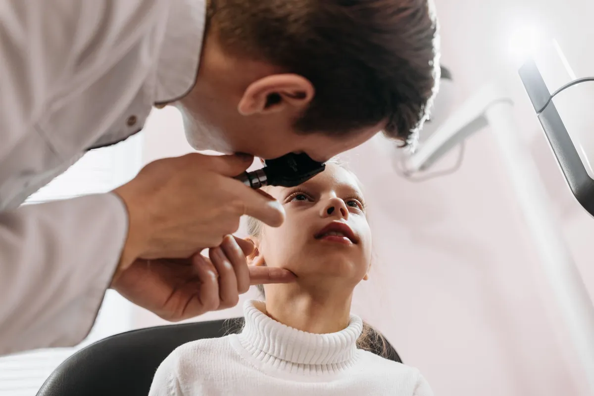 Doctor examining a child’s throat with an otoscope in a clinical setting.