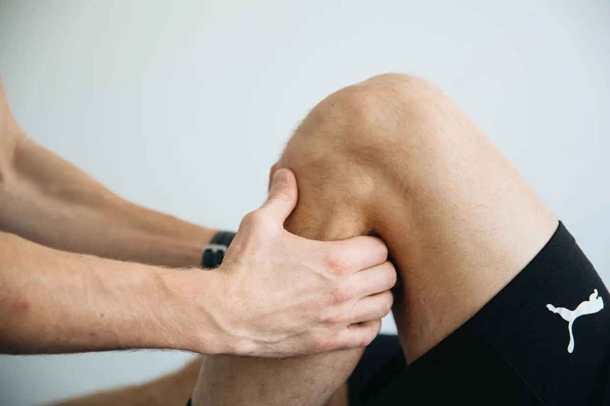 Person applying pressure to a knee, demonstrating injury prevention techniques.