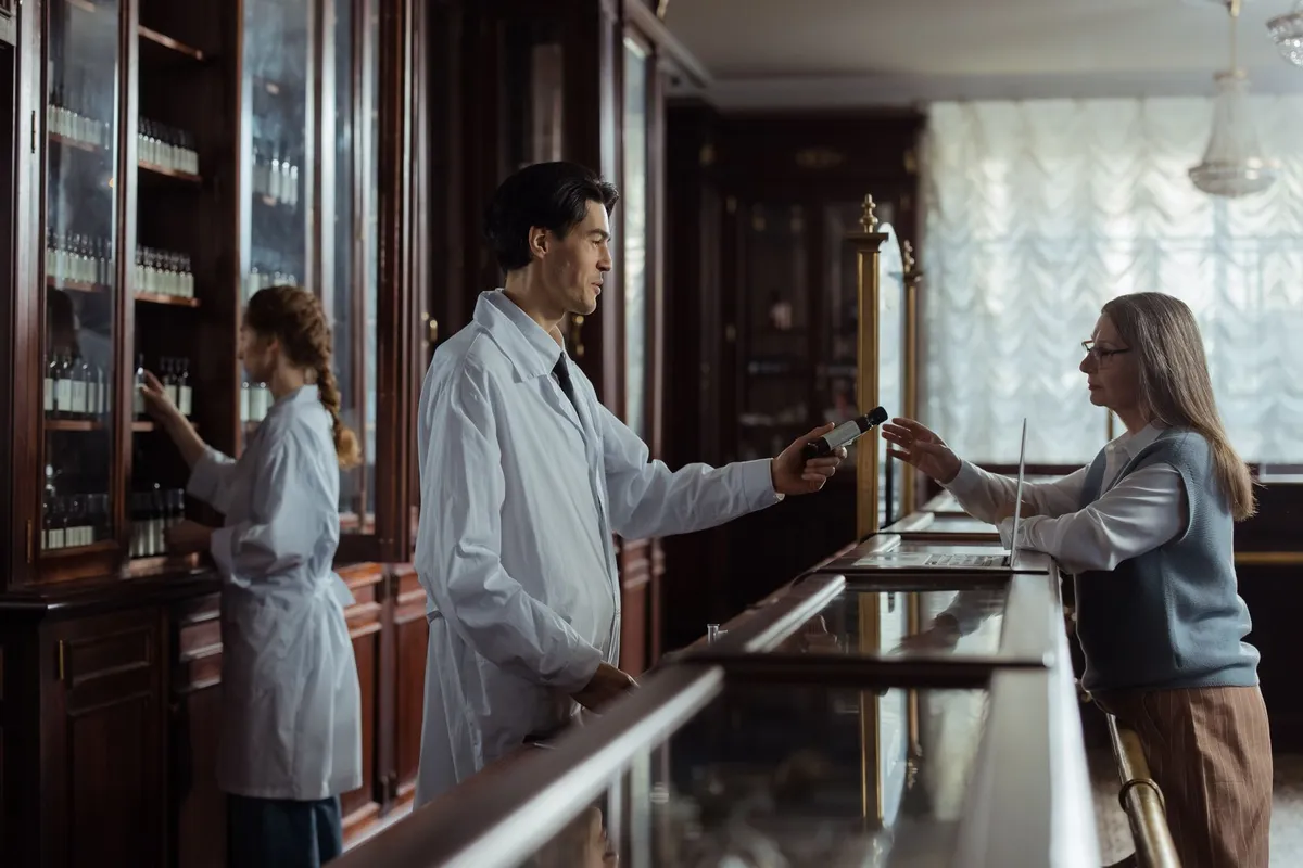 Pharmacist handing a product to a customer at a pharmacy counter.