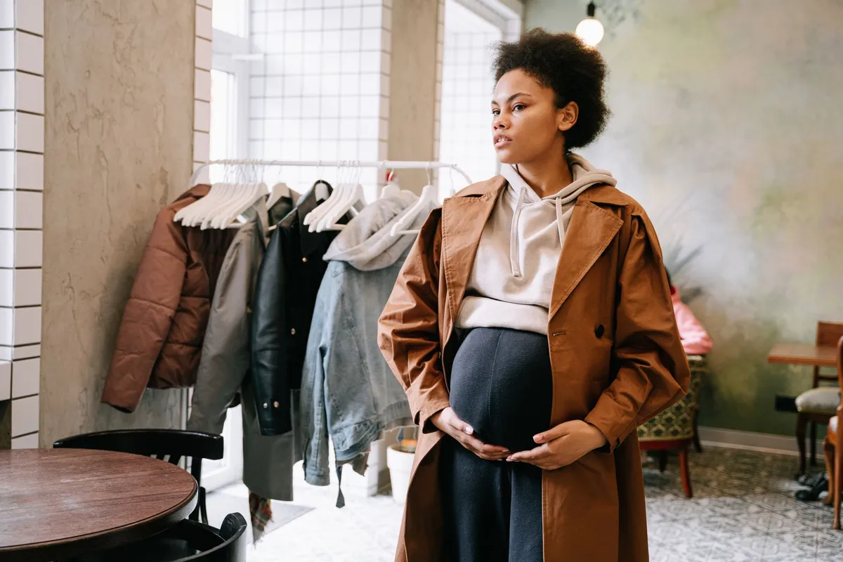 Pregnant woman in a store, gently holding her belly while looking thoughtful.