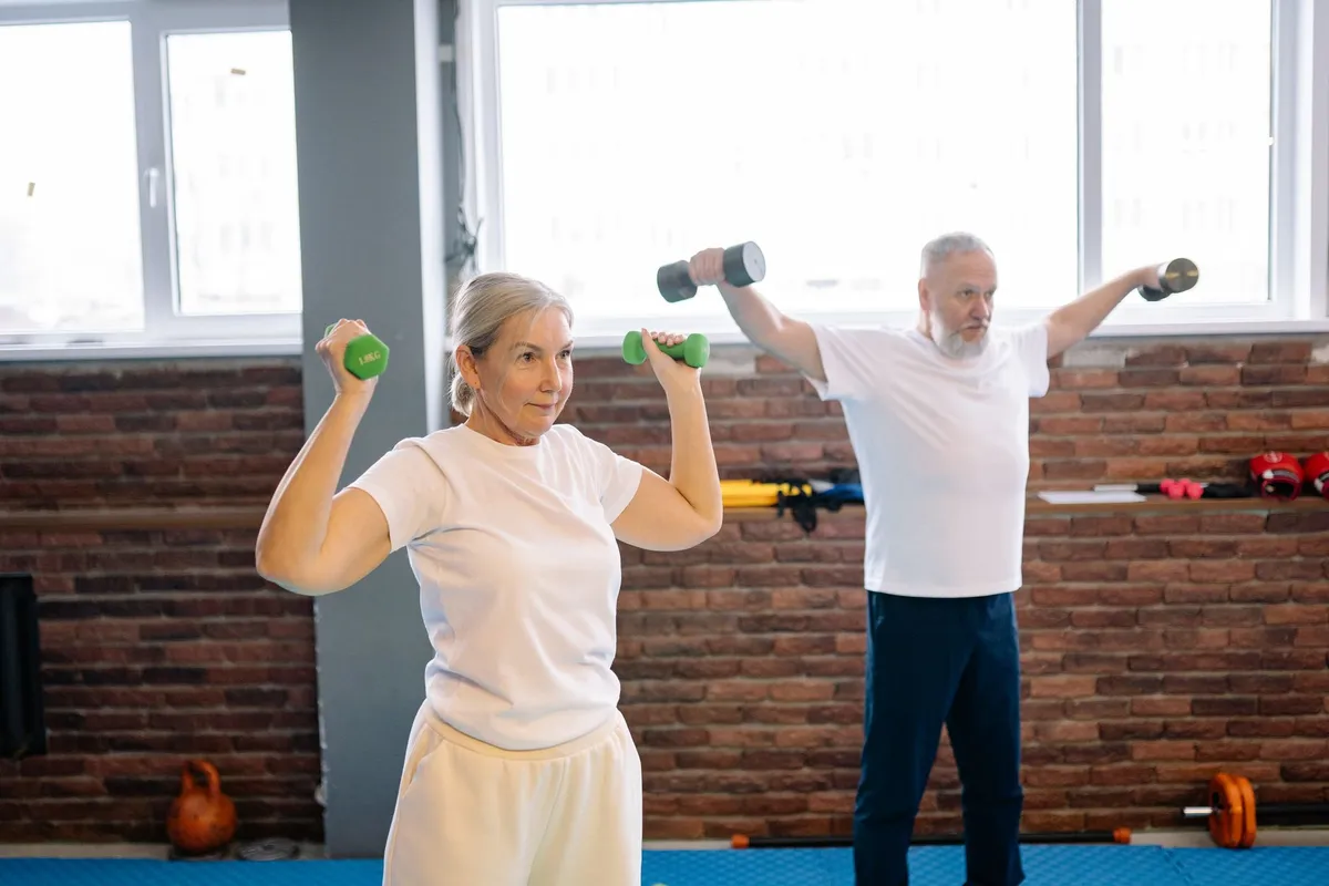 Senior woman lifting weights with a partner in a gym setting.