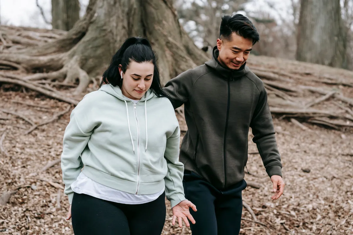 Two people walking together in a park, one providing support to the other.