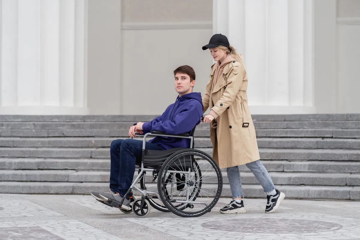 A wheelchair being pushed up steps by a person in a coat.