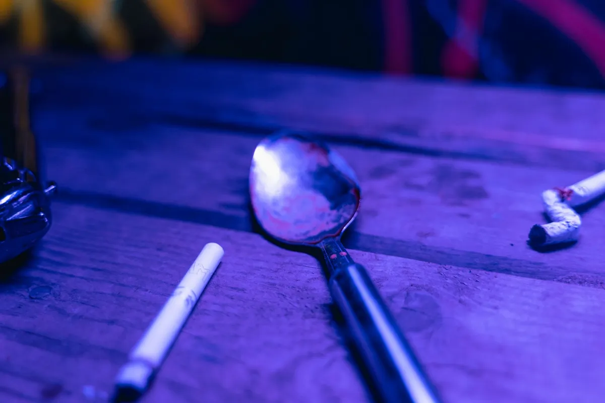 A spoon with residue and cigarette butts on a table, suggesting drug use context.