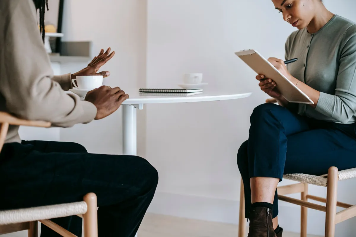 Counselor taking notes while client gestures during a discussion.