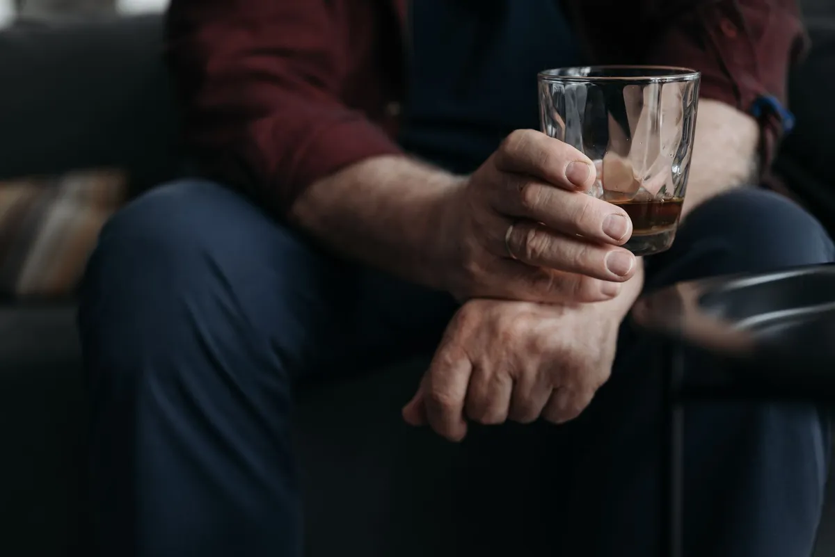 Close-up of a person holding a glass of whiskey in a casual setting.