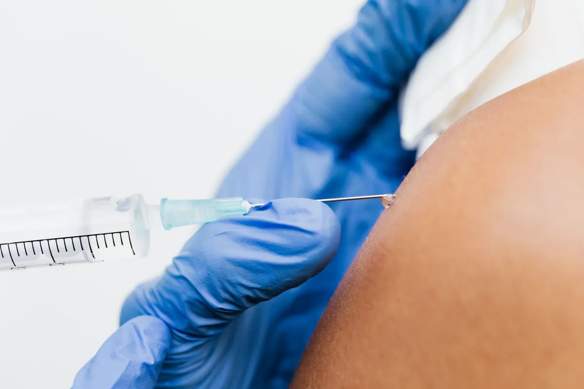 Close-up of a syringe injecting into a person’s shoulder, illustrating vaccination.