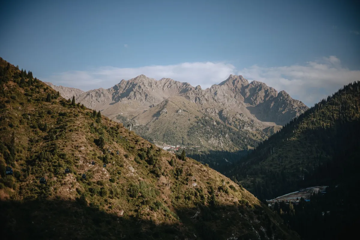 Mountain range with rocky peaks and green hills in the foreground.