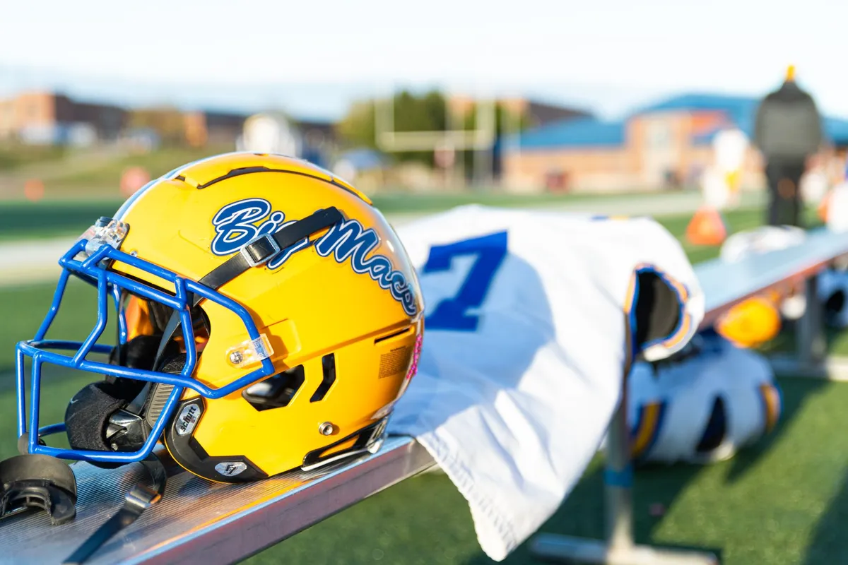 Close-up of a football helmet and jersey on a bench at a sports field.