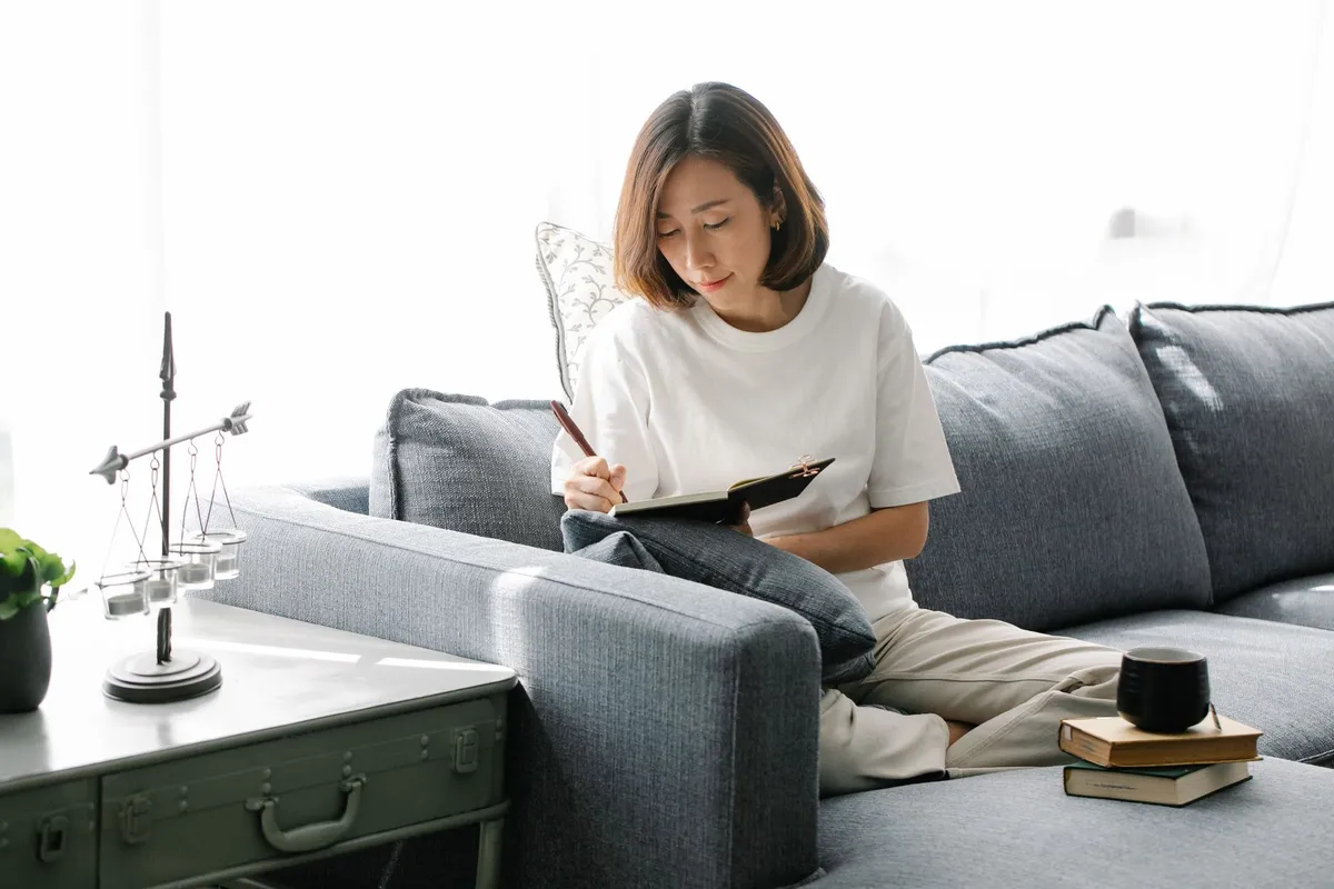 Woman journaling on a couch in a bright living room.