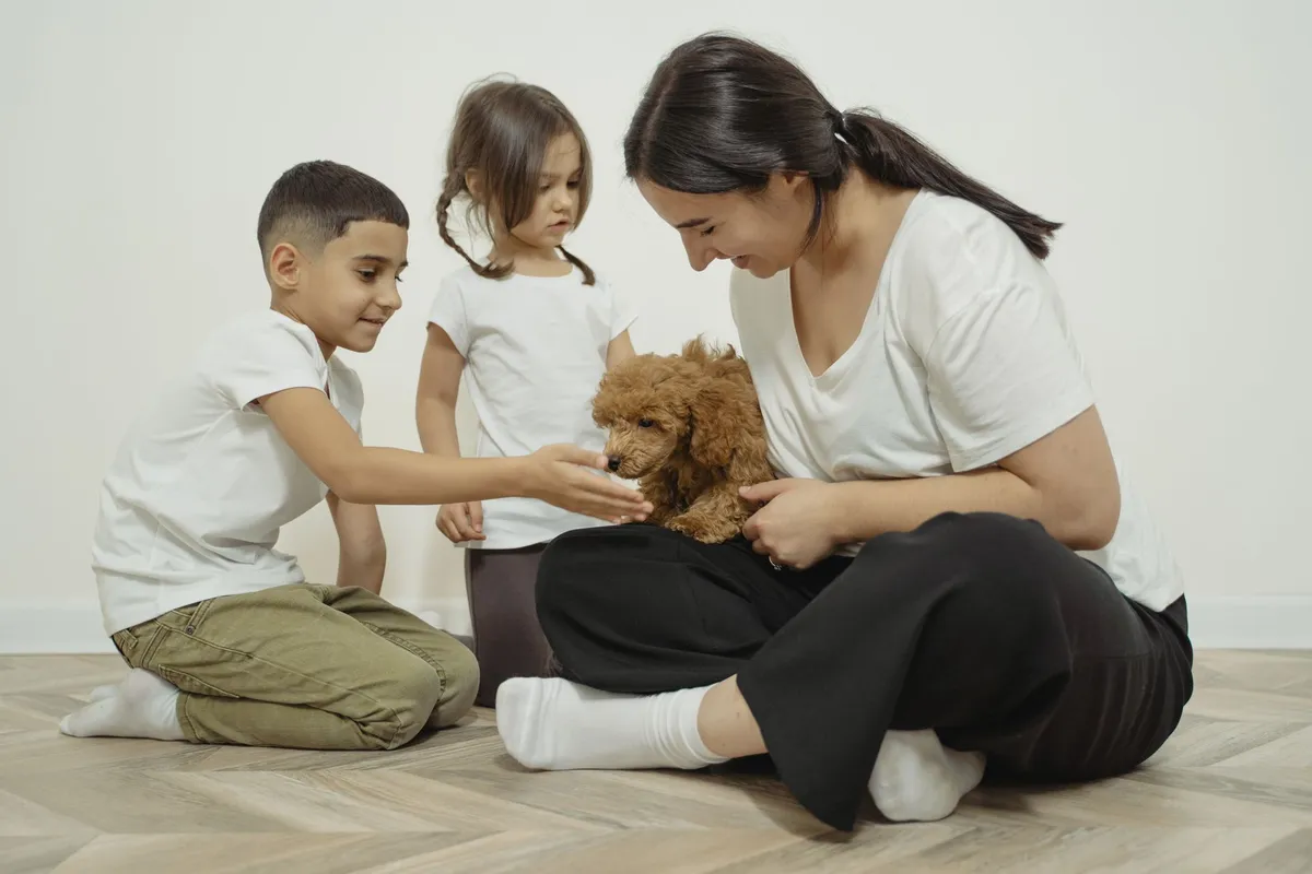 Two children interacting with a small dog while a parent supervises them.