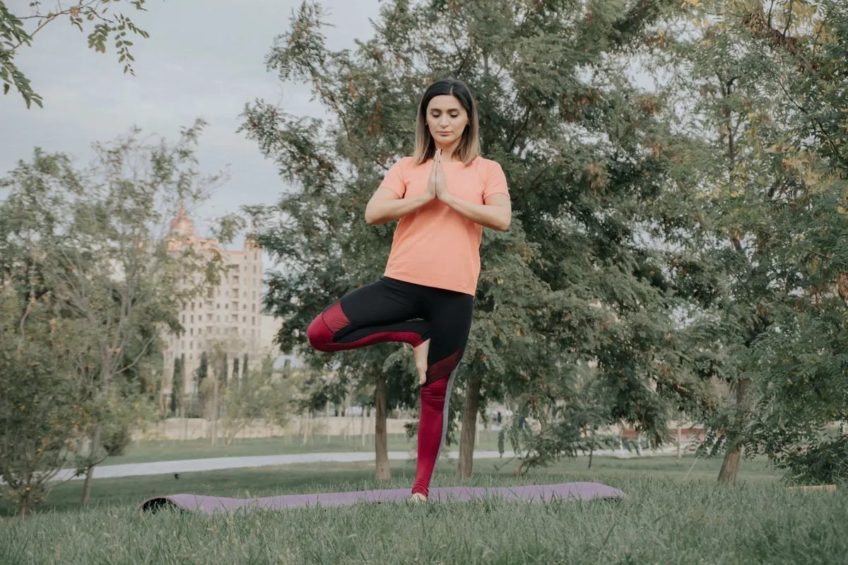 Woman practicing yoga in a park, balancing on one leg with hands in prayer position.