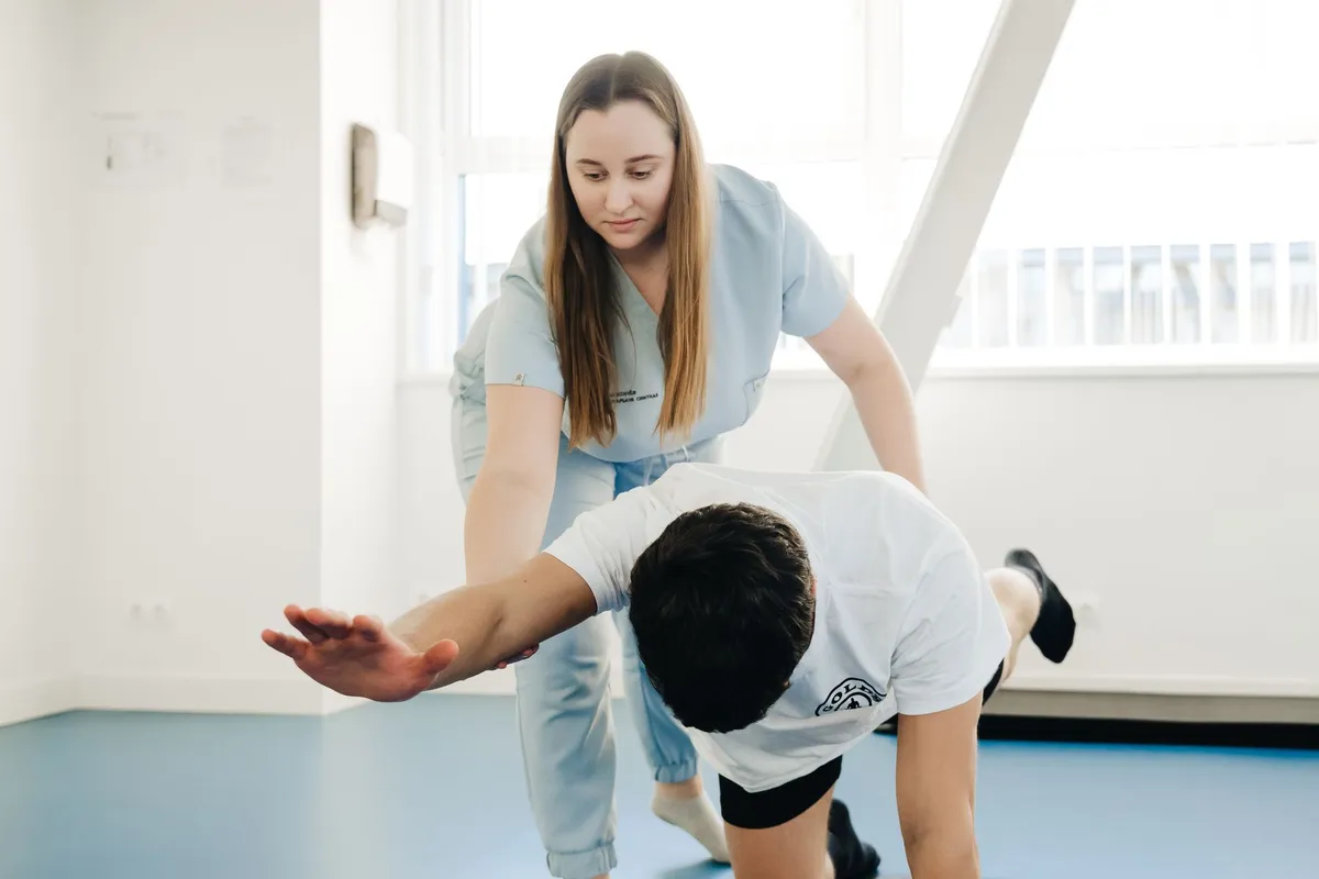 Physical therapist guiding a patient in a spine exercise on hands and knees.
