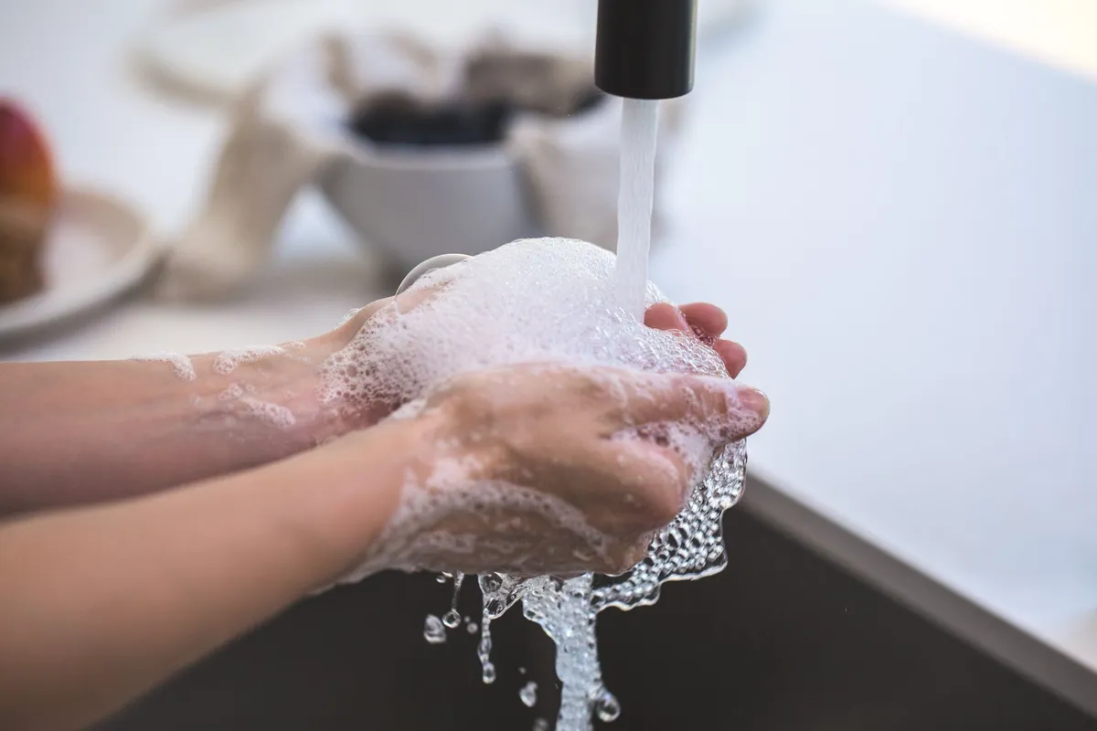Hands lathered with soap under running water at a sink.