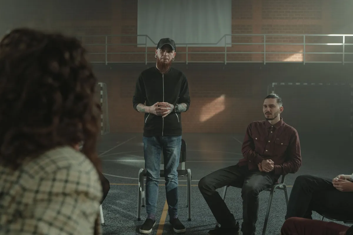 A man speaking to a group of men in a support group setting.