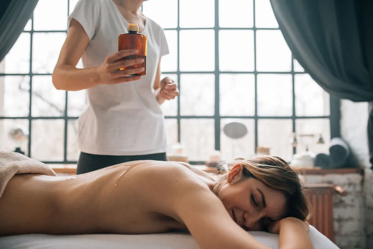 Massage therapist holding essential oil bottle over client on a massage table.