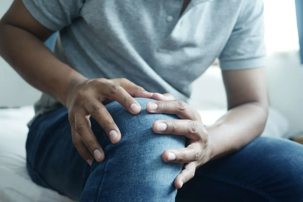Person sitting and holding their knee, indicating discomfort or pain.