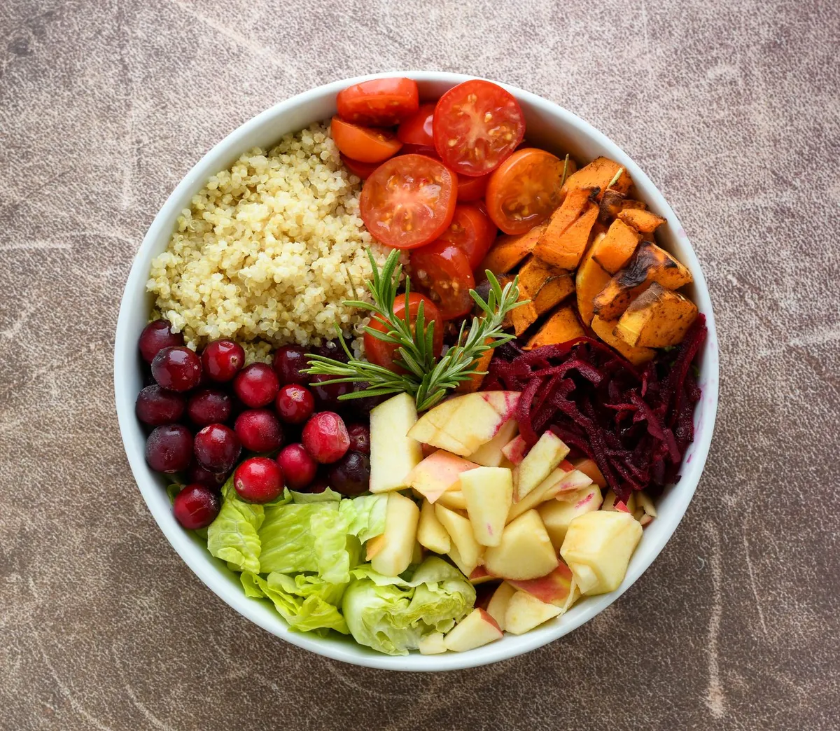 A colorful bowl of quinoa, tomatoes, sweet potatoes, and fruits, showcasing healthy ingredients.