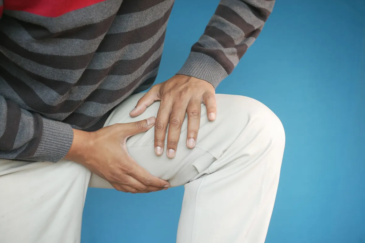 Person holding their knee, indicating discomfort, against a blue background.