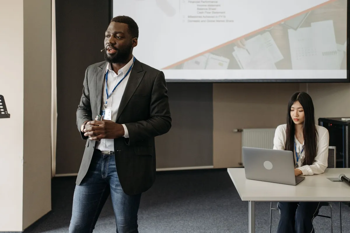 A man confidently speaking in front of a group during a presentation.