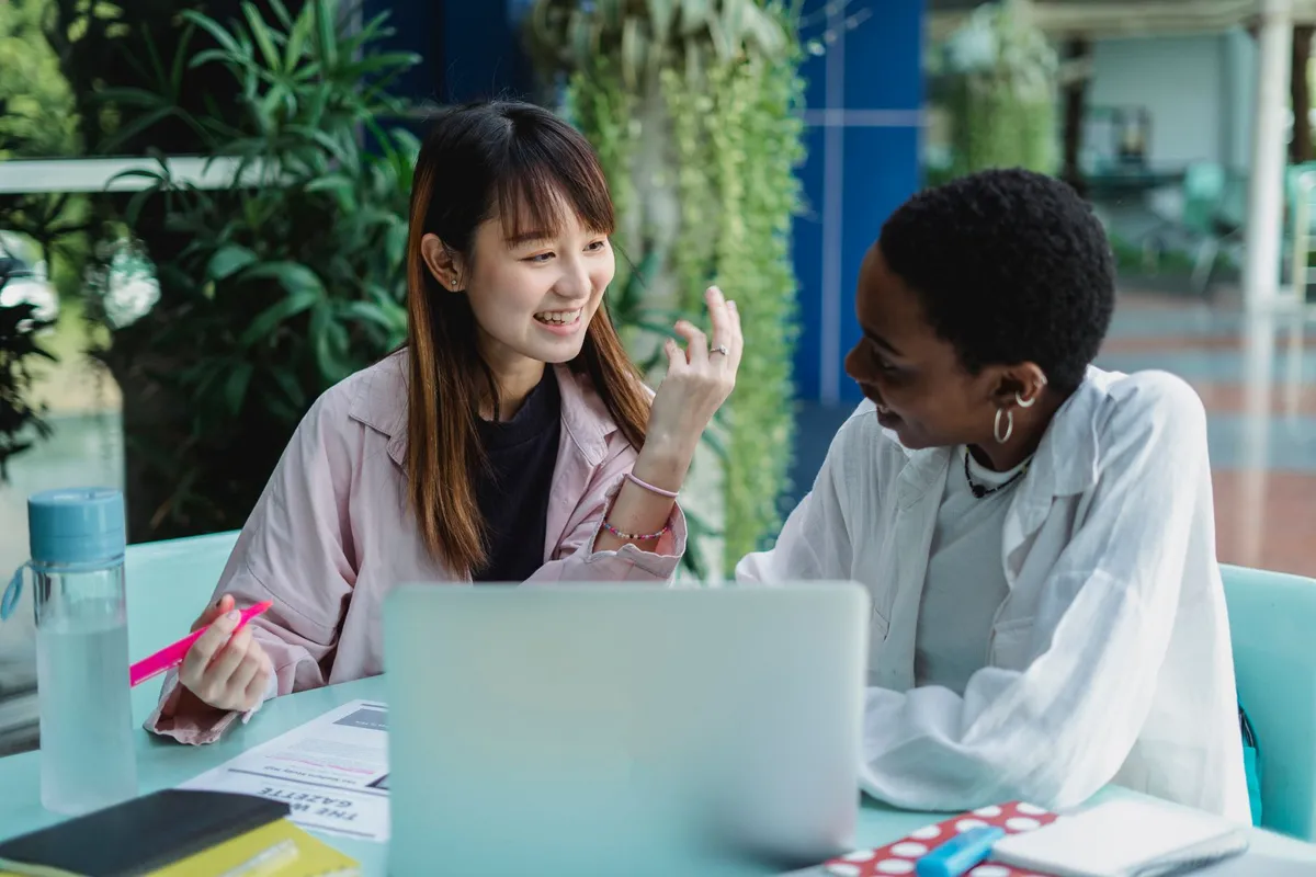 Two women engaged in a conversation at a table with a laptop and documents.