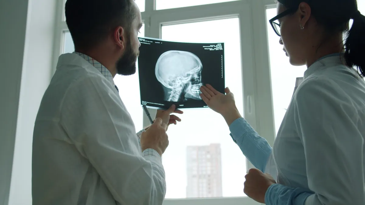 Two doctors examining an X-ray of a human skull in a clinical setting.