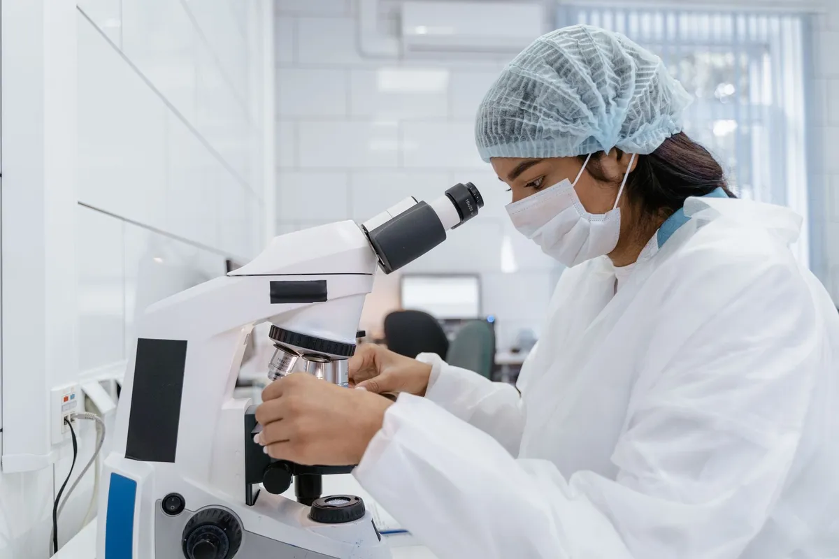Laboratory technician using a microscope in a clinical setting.