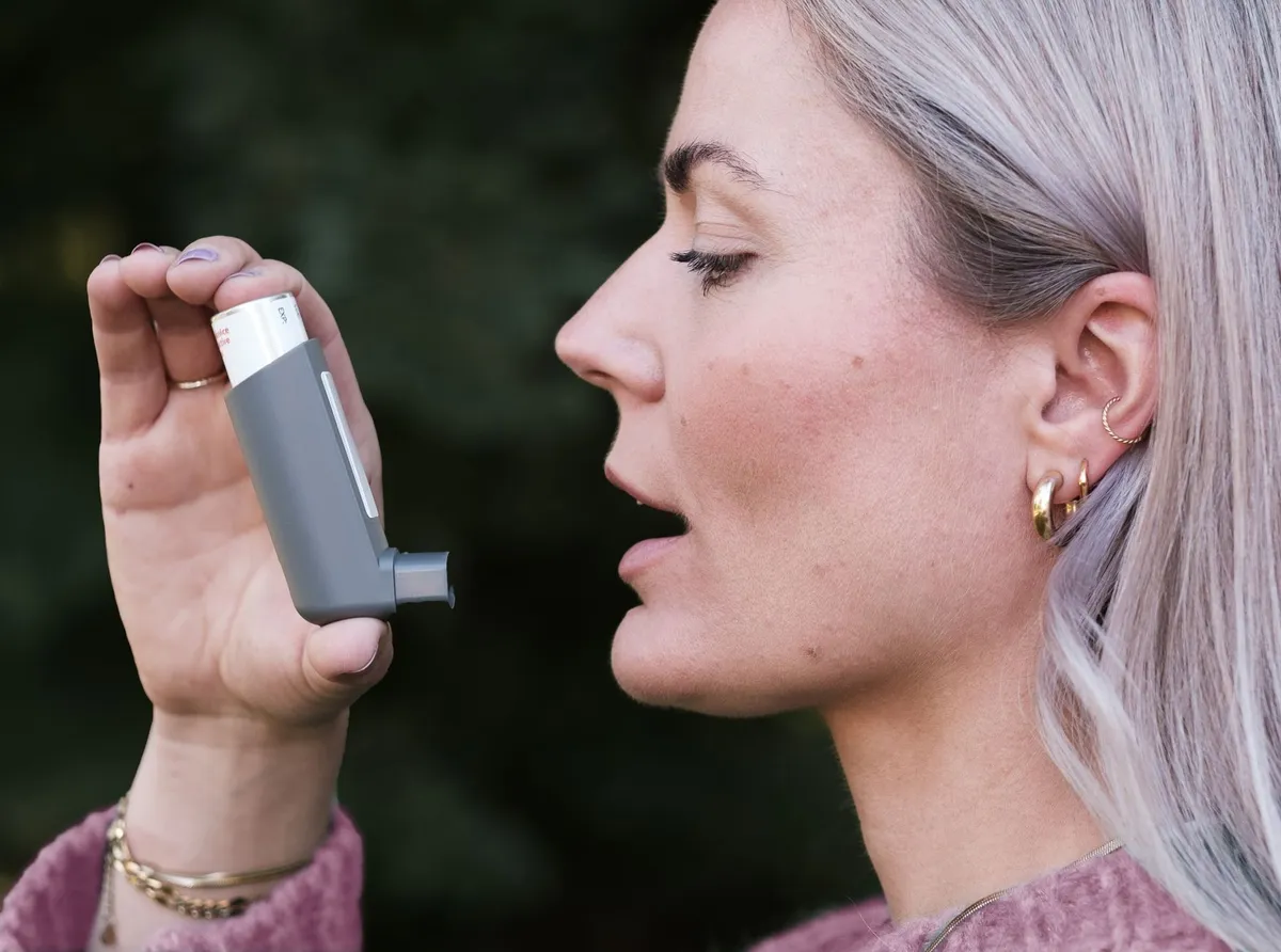 Person using an inhaler outdoors, demonstrating asthma management.