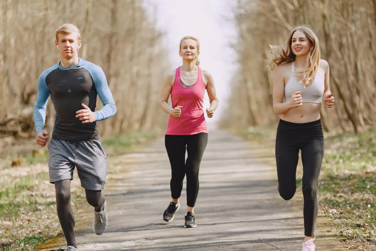 Three adults jogging on a path surrounded by trees in a park.