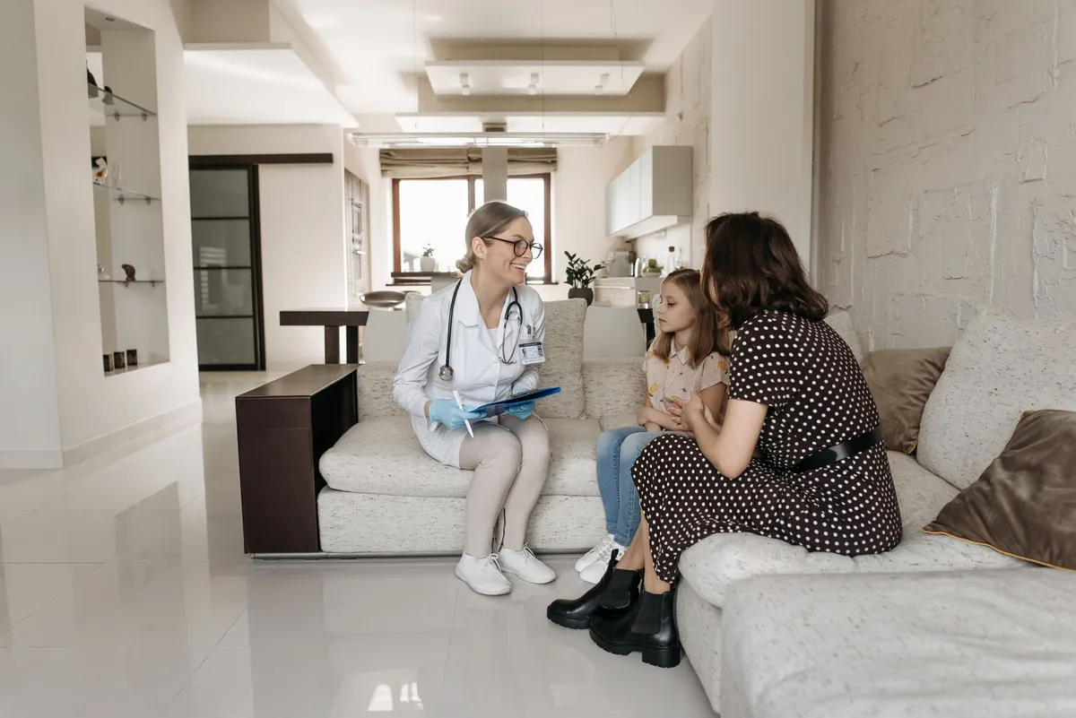 Doctor discussing health with a mother and daughter in a living room setting.