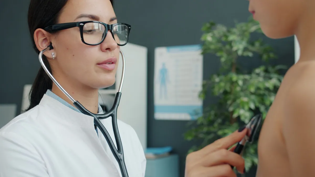 Pediatrician using a stethoscope on a child’s back in a clinic setting.