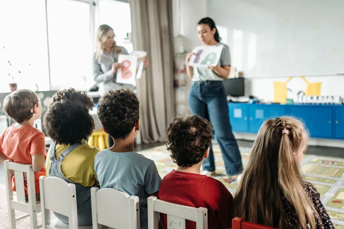 Teacher showing letters to children in a classroom setting.