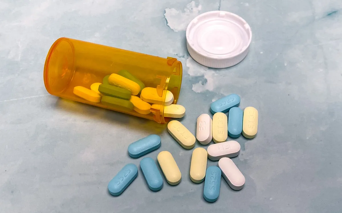 Prescription bottle with blue and yellow pills spilled on a surface