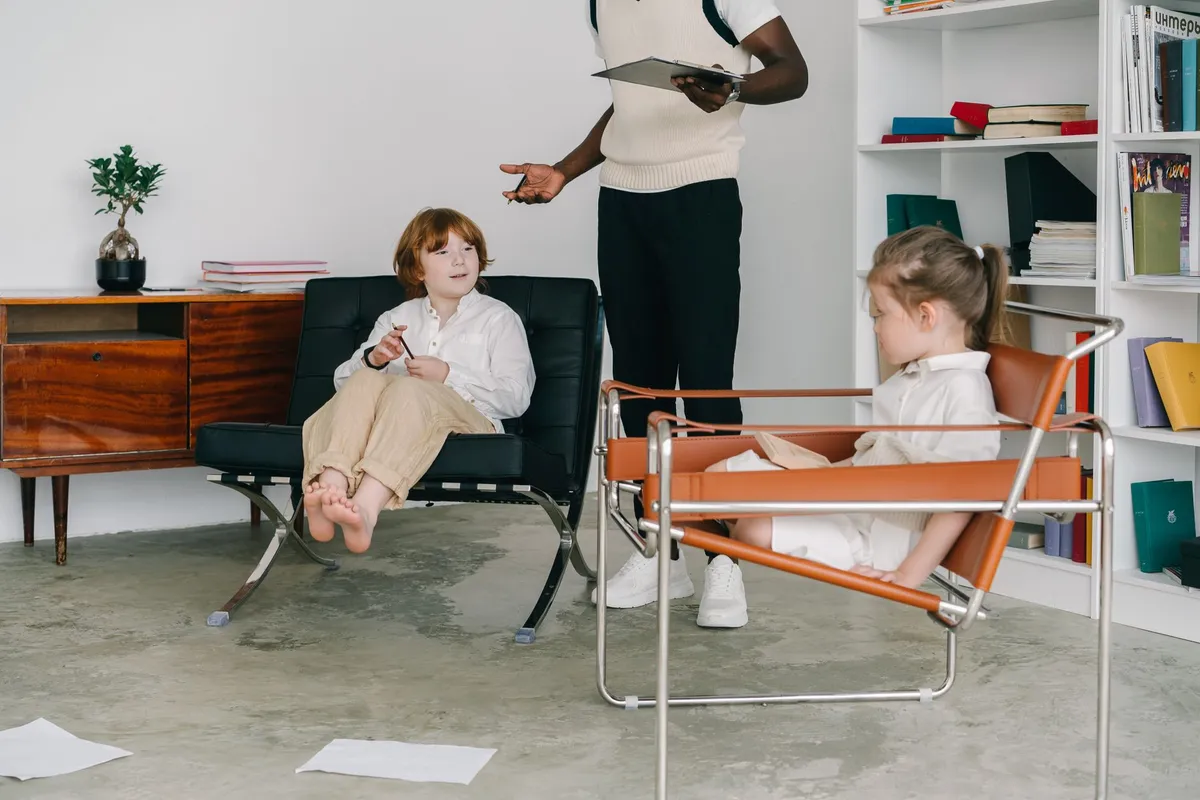 Two children in a therapy session with an adult facilitator nearby.