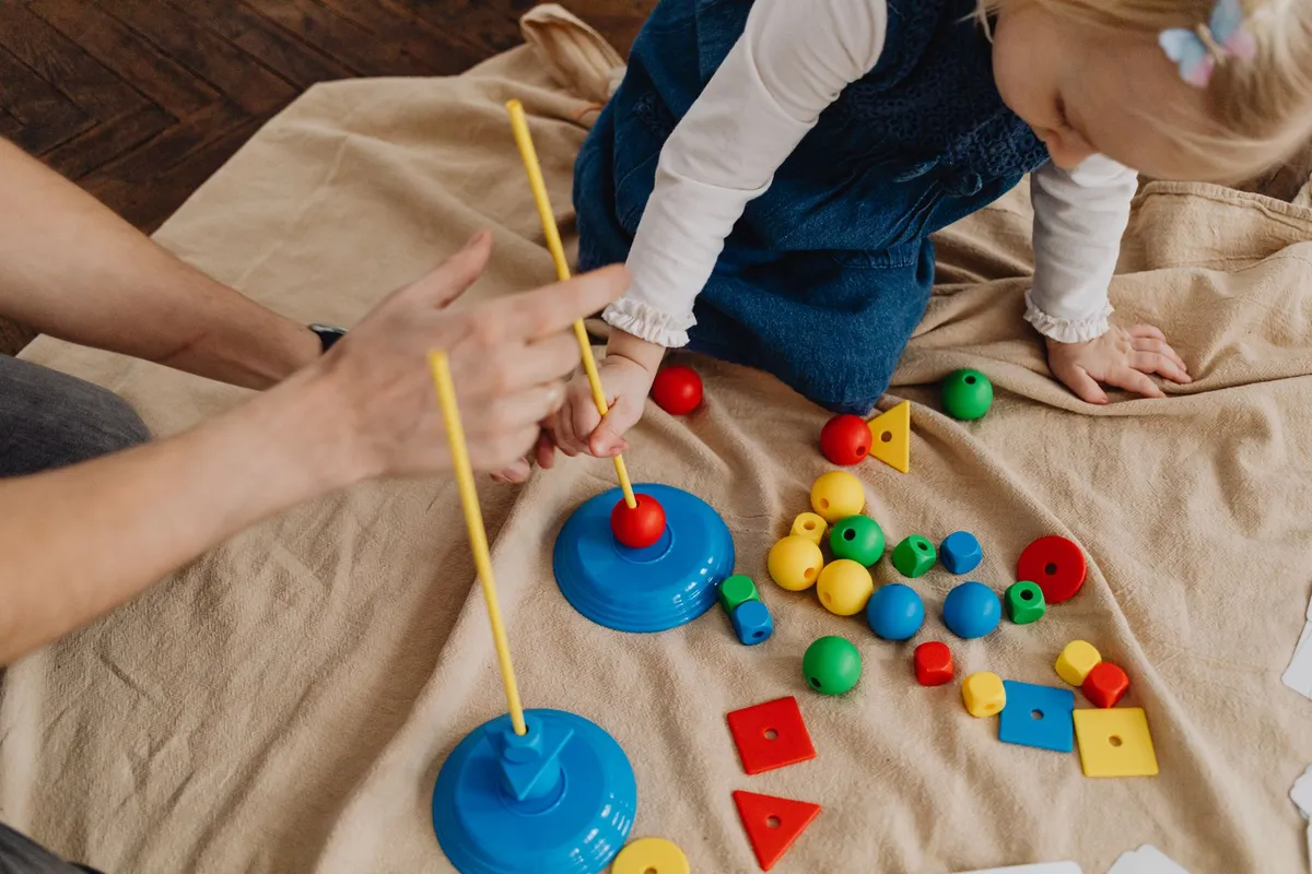 Child playing with colorful geometric shapes and a caregiver in a therapy setting.