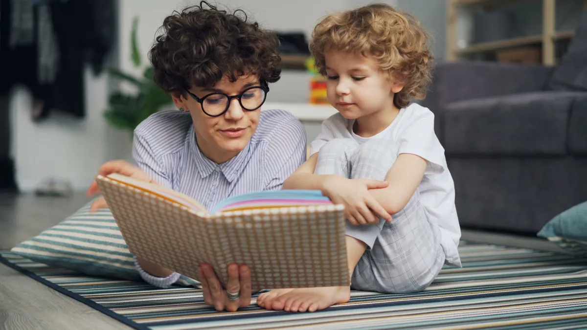 Adult reading a book to a child on a rug in a cozy living room.