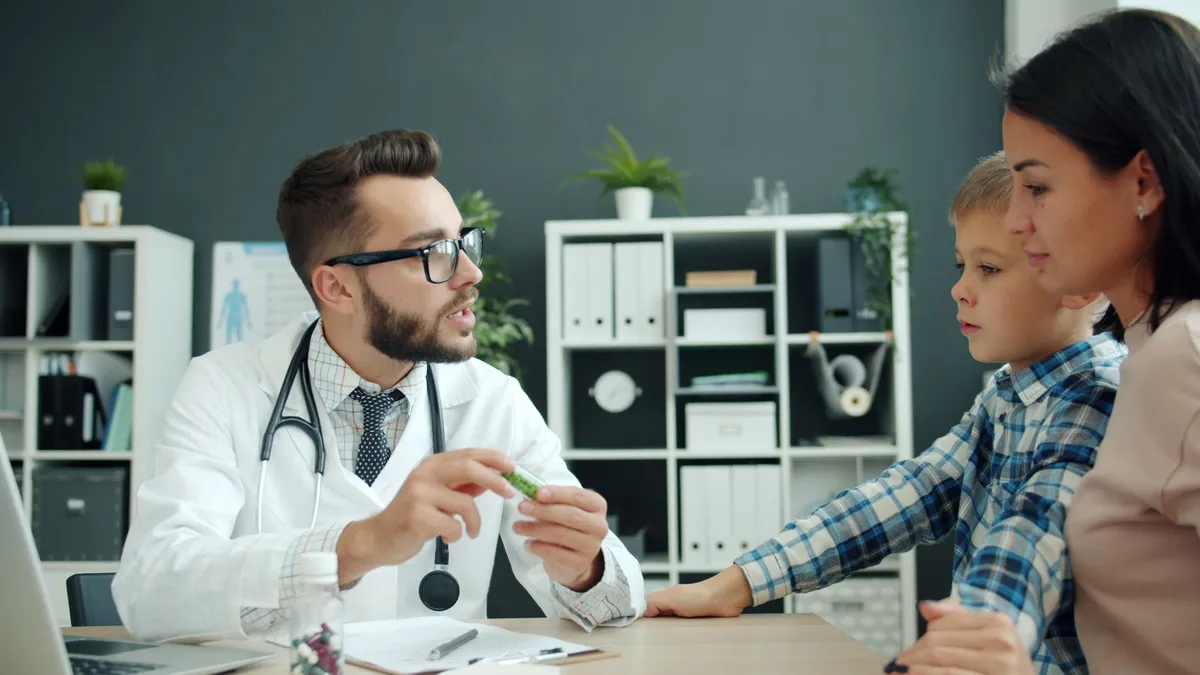 Pediatrician discussing medication with a mother and her son in a clinical setting.