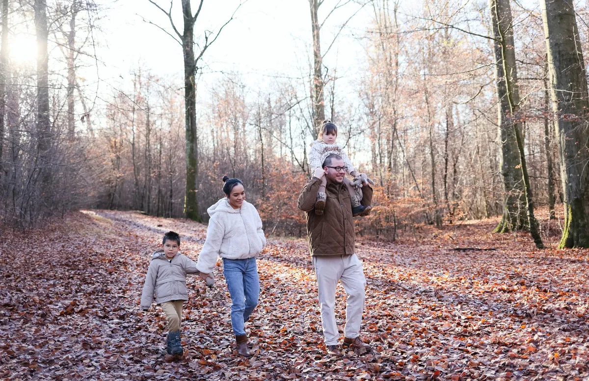 Family walking on a forest path with autumn leaves, illustrating outdoor activities.