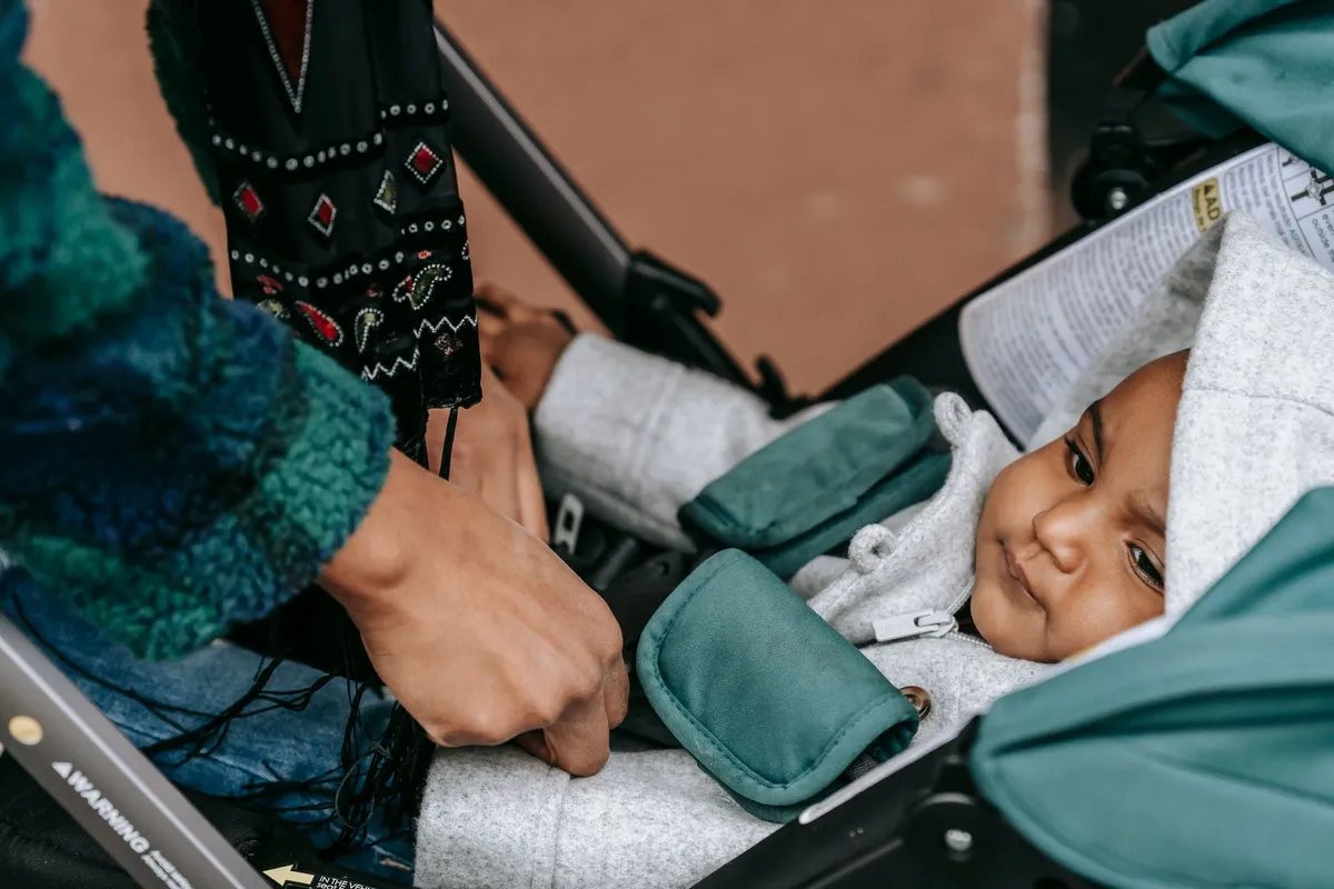 Parent fastening a baby into a stroller with safety straps.