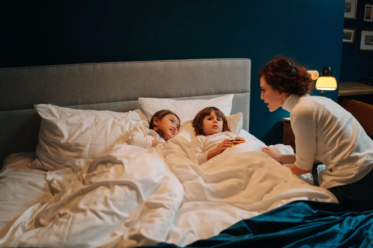 Two children in bed with a caregiver, discussing bedtime stories and comfort items.