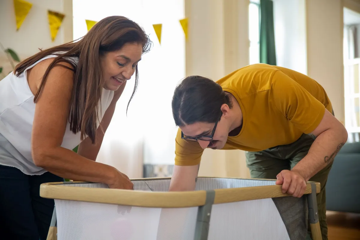 Two adults assembling a baby crib together in a bright room.