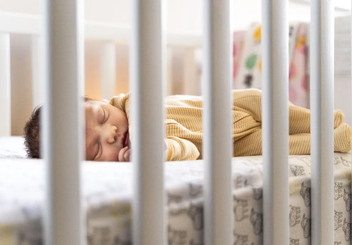 Infant sleeping peacefully in a crib with safety standards visible.