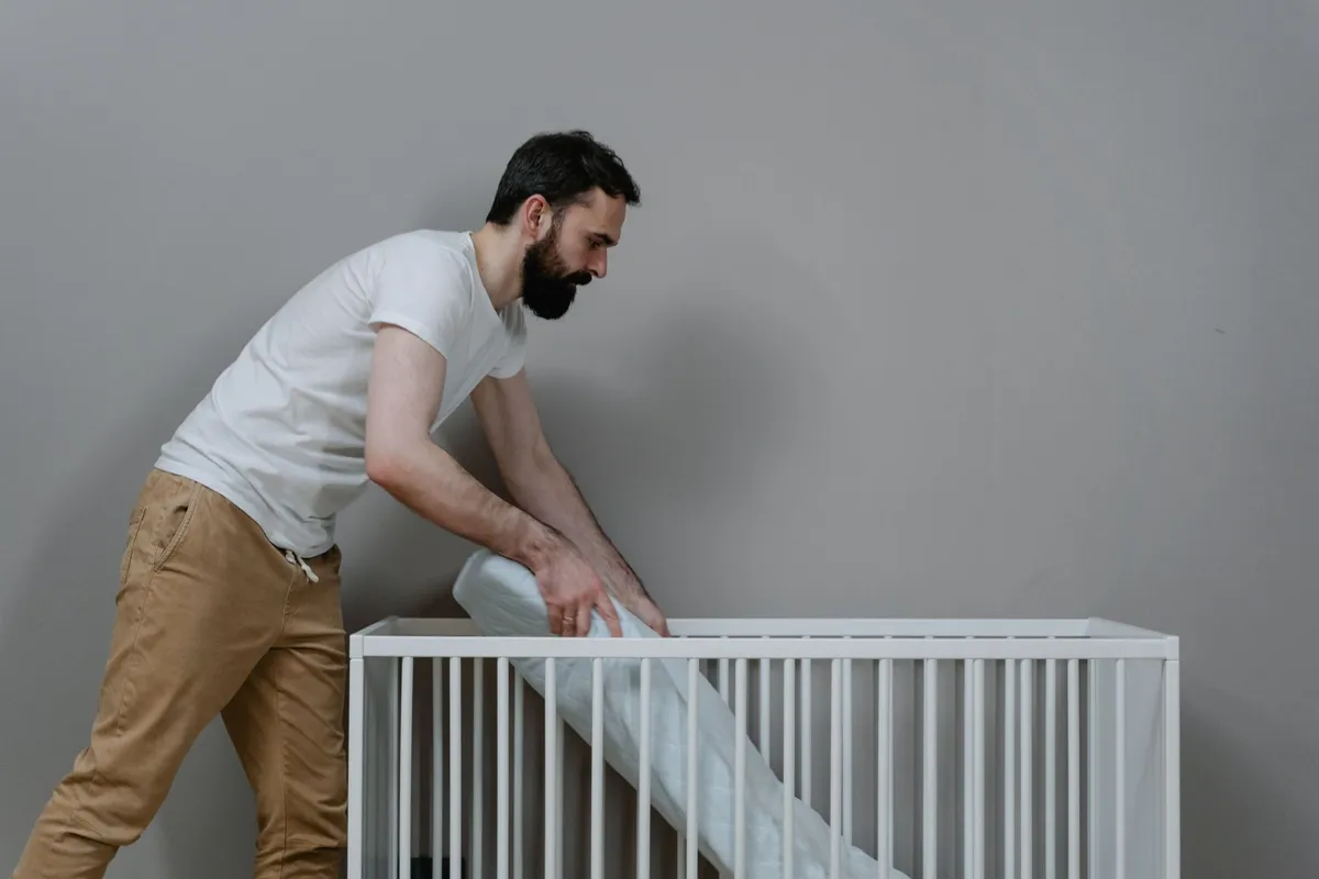 Person placing a mattress in a crib, illustrating crib setup and safety.
