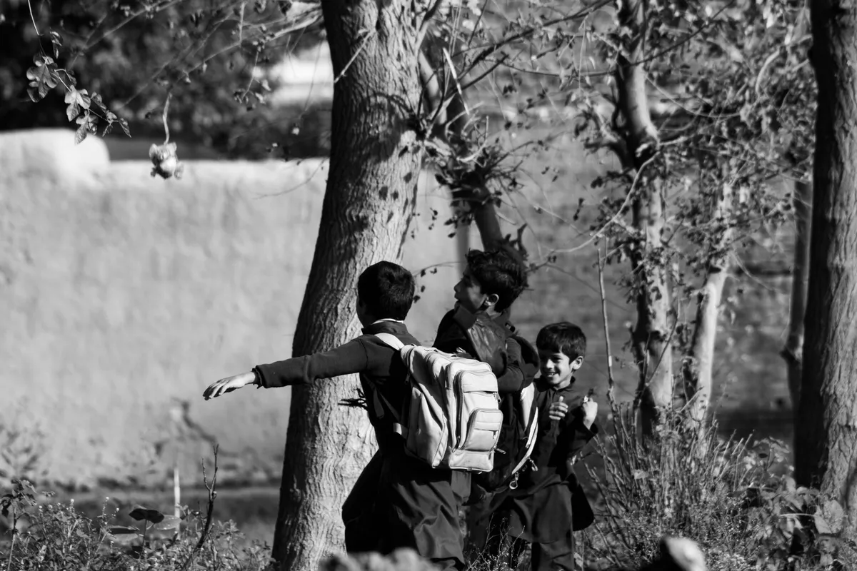 Three children playing outdoors with backpacks near trees.