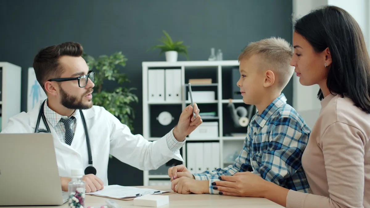 Pediatrician discussing health with a child and parent in a clinic setting.